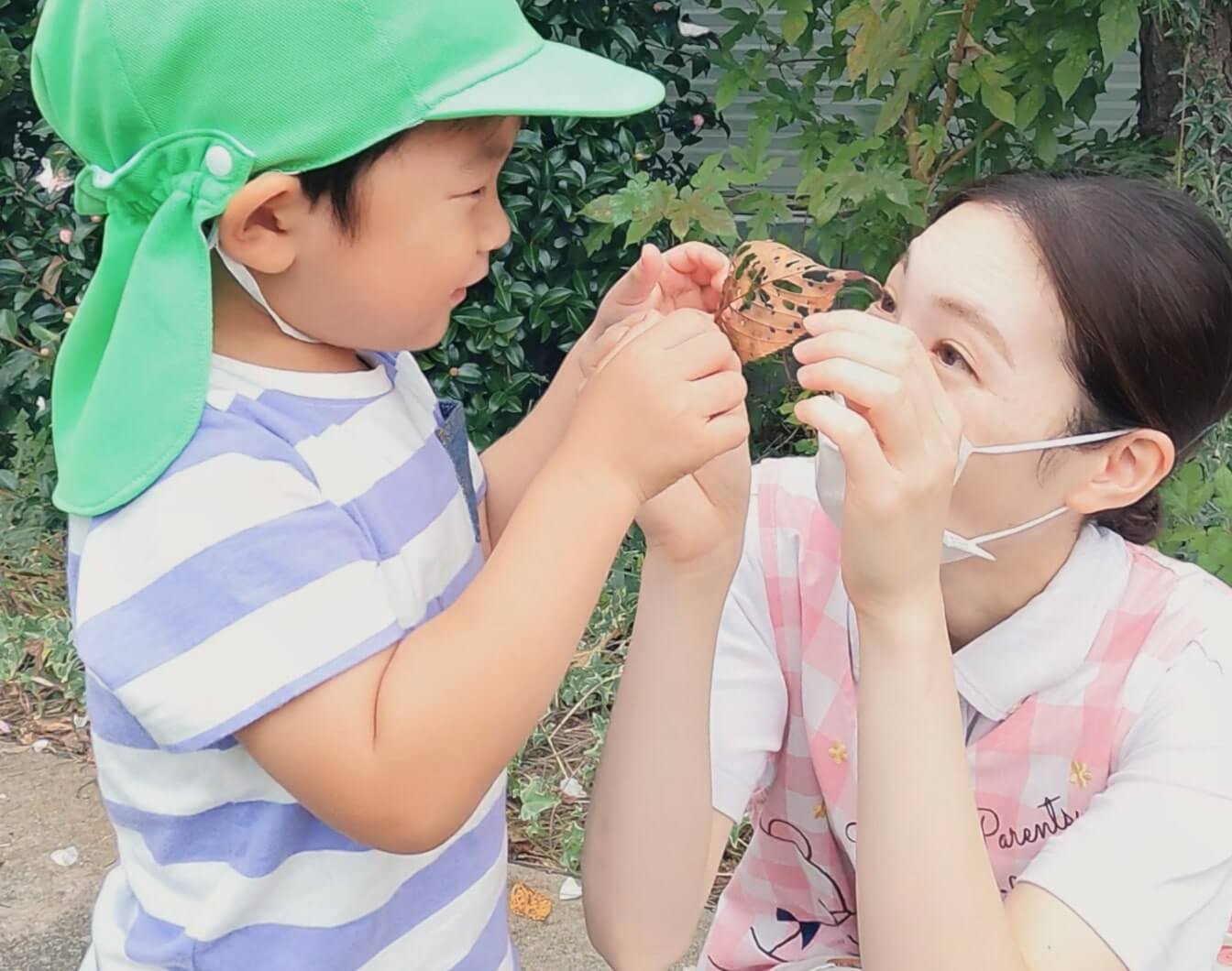 子どもと先生が、珍しい落ち葉を一緒に拾い上げている様子